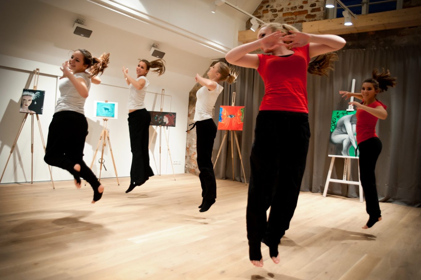 Gruppe von Frauen beim Tanztraining in hellem Studio, Sprungbewegung sichtbar.
