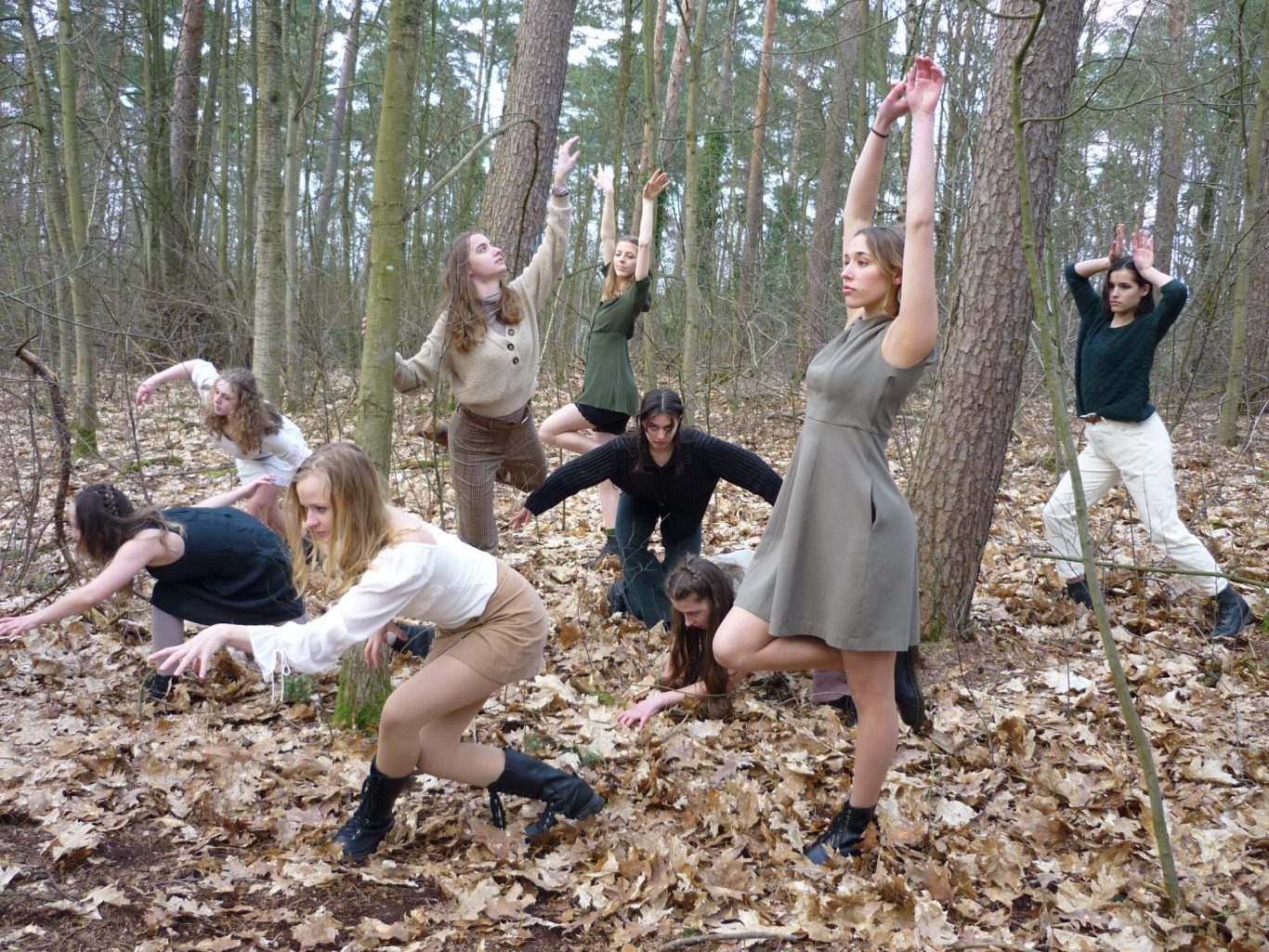 Neun Personen in Wald zwischen Laubblättern, in verschiedenen tänzerischen/ausdrucksvollen Posen.