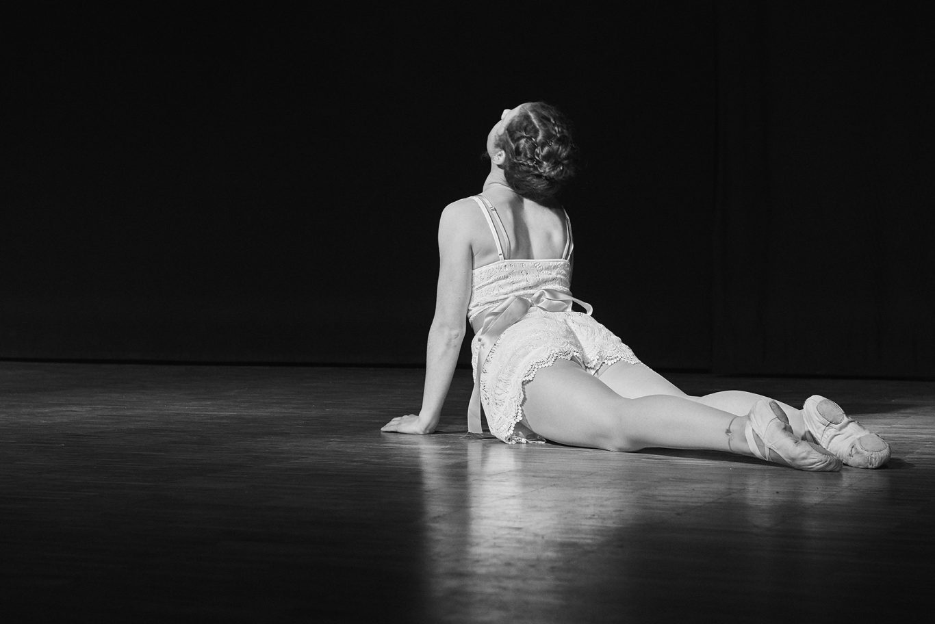 Ballerina liegt auf Bühne, Oberkörper hochgestützt, Scheinwerferlicht.