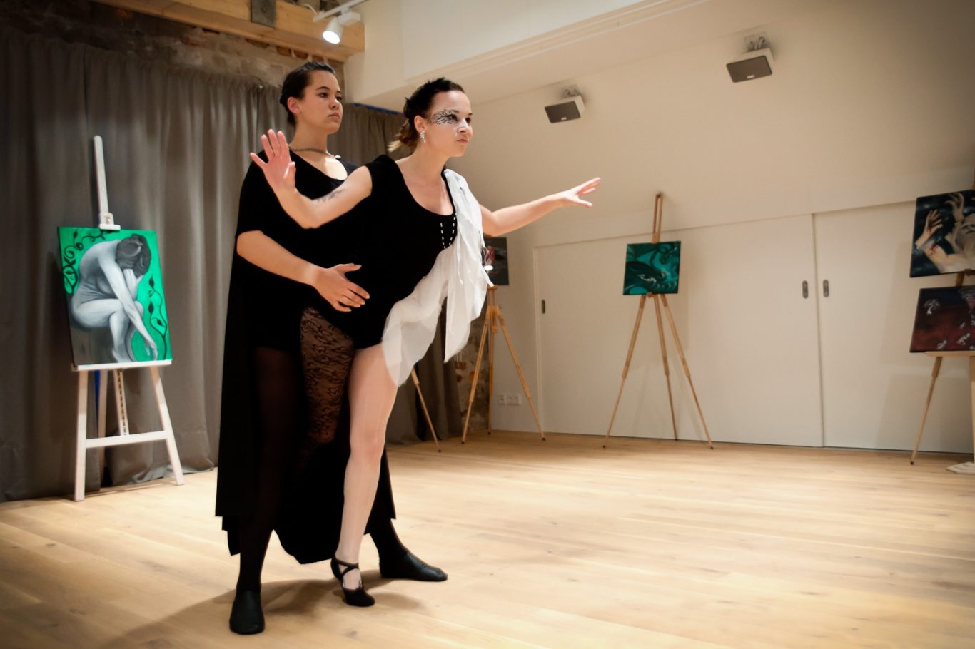 Drei Tänzerinnen in Ballettkleidung üben in hellem Tanzstudio vor Staffeleien und Gemälden.