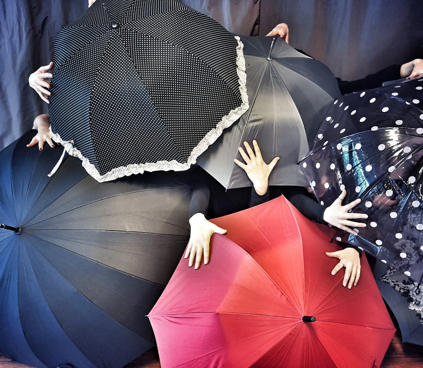 Aufsicht auf mehrere geöffnete Regenschirme in verschiedenen Farben, Hände dazwischen sichtbar.