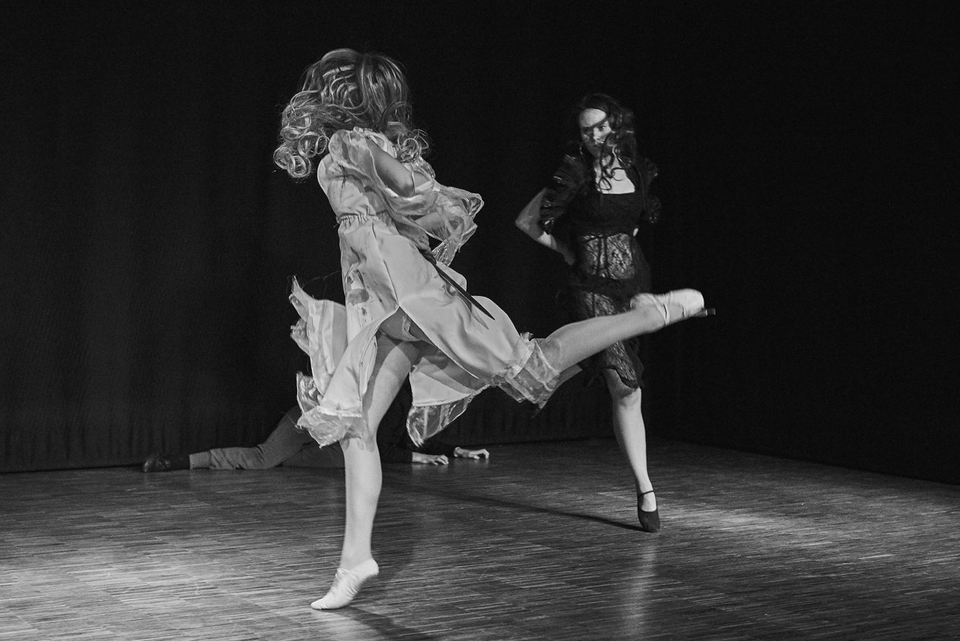 Zwei Balletttänzerinnen in schwarzen und hellen Kostümen beim Sprung auf einer Bühne.